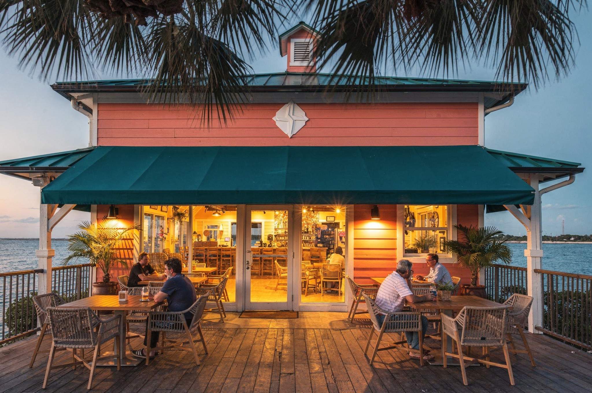 Fictional waterfront restaurant with a teal awning, warmly lit windows, and an outdoor dining terrace.